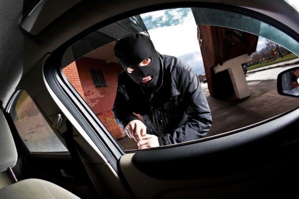 A man in a black mask peers out the car window, illustrating vehicle safety in A Guide to Keeping Vehicles Safe From Thieves.