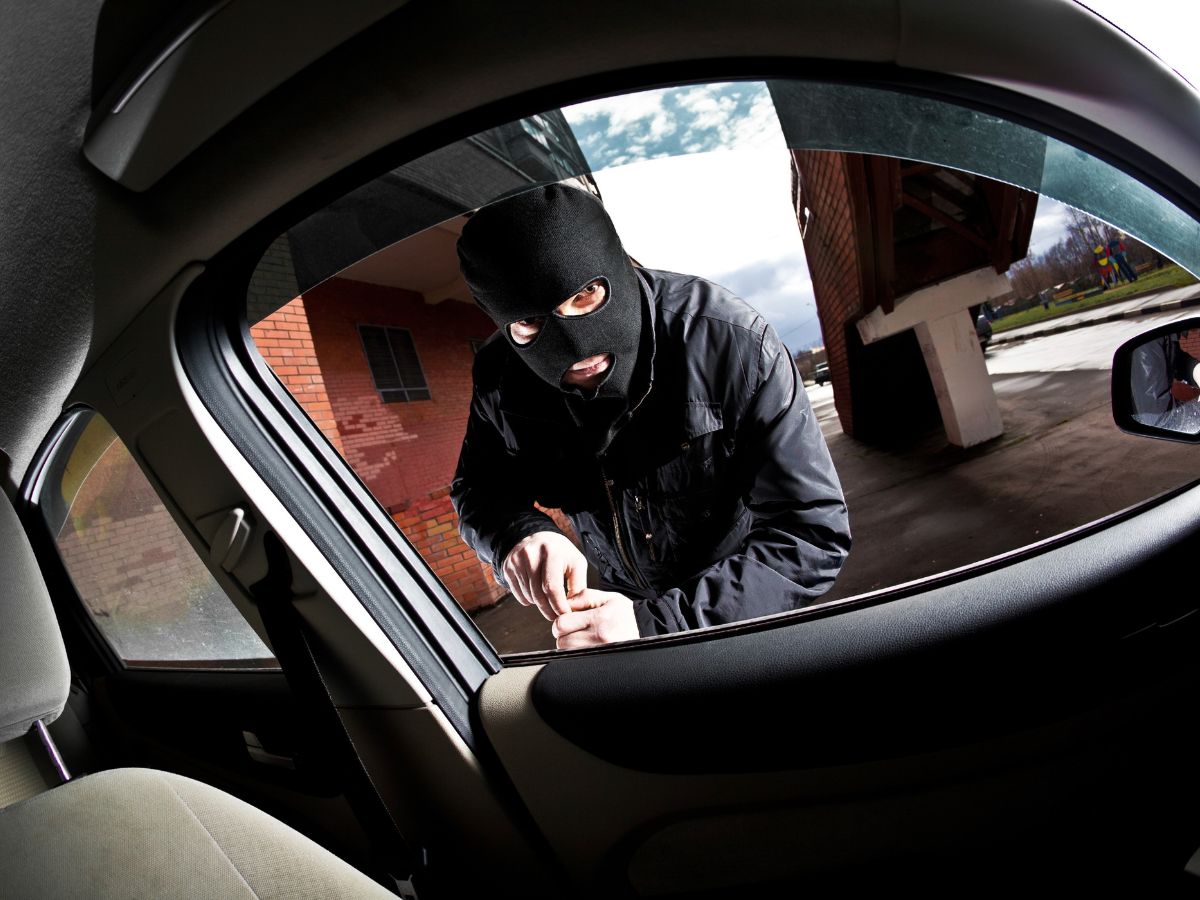 A man in a black mask peers out the car window, illustrating vehicle safety in A Guide to Keeping Vehicles Safe From Thieves.