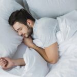 A man peacefully sleeping in a bed with crisp white sheets, enjoying the benefits of linen bedding for a better sleep.