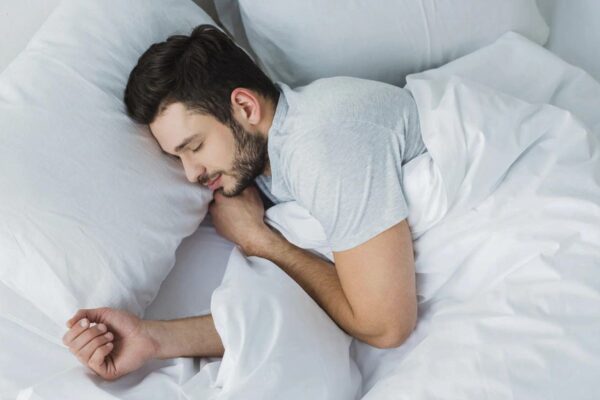 A man peacefully sleeping in a bed with crisp white sheets, enjoying the benefits of linen bedding for a better sleep.